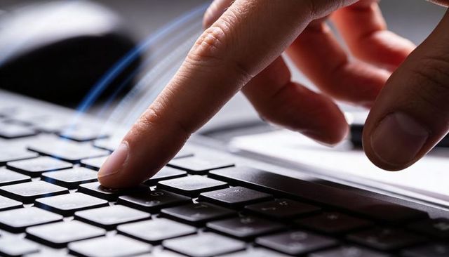 Right index finger pressing laptop key close-up showing typing precision and focus