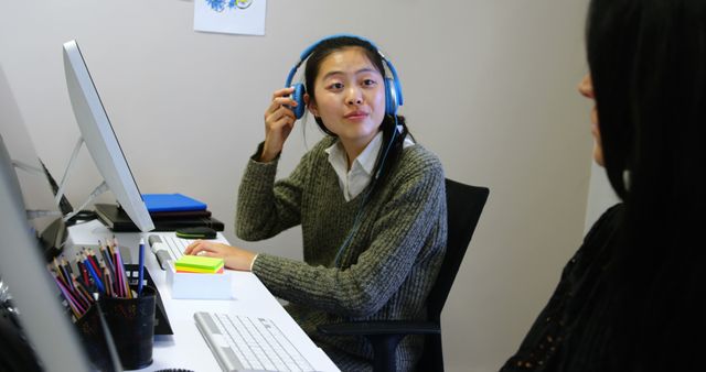 Young Asian Woman in Office Working on Desktop Computer with Headphones - Download Free Stock Photos Pikwizard.com