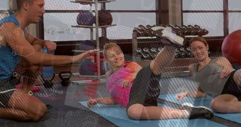 Kneeling trainer guiding client lifting leg on blue mat during small group gym training
