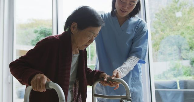 Smiling asian female doctor helping senior female patient to walk using walking frame. senior health and healthcare services.