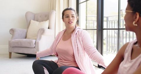 African american friends stretching and chatting in pink activewear by glass doors