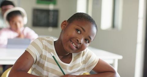 Smiling African American Girl Writing and Learning in Bright Modern Classroom