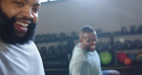 African men laughing and lifting weights together in gym with dumbbells