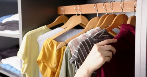 Hand Selecting Clothing from Organized Wooden Closet Rod
