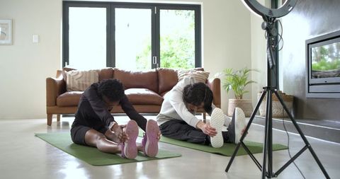 Man and african american woman stretching on mats in modern living room for home workout