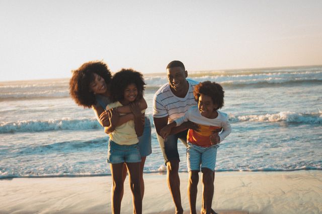 Portrait of happy african american parents and children embracing on beach at sunset. summer beach vacation by the sea.
