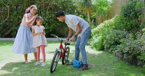 Father Adjusting Daughter's Bicycle in Sunny Backyard