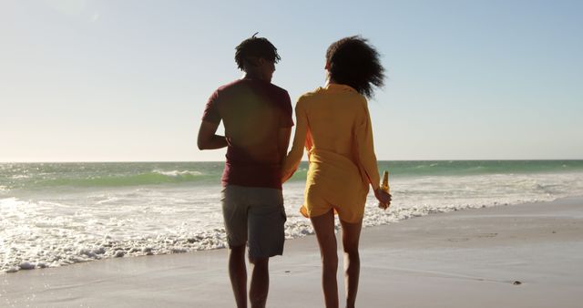 African american couple walking, holding hands and bottles on sunny beach with copy space - Download Free Stock Photos Pikwizard.com
