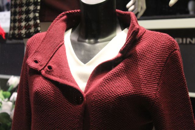 Mannequin dressed in an elegant red knit coat over a white top is perfect for showcasing winter fashion in retail stores. Ideal for use in fashion blogs, online clothing shops, and promotional materials for winter clothing collections.