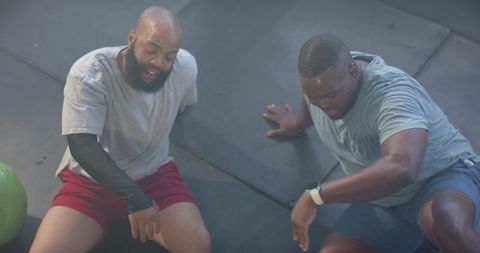 Two men resting after intense workout on gym mats with exercise ball and smartwatch