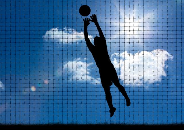 Silhouette of an athlete jumping to catch a ball against a bright sky with clouds and a net in the background. Ideal for use in sports-related content, motivational posters, fitness blogs, and advertisements promoting athletic gear or outdoor activities.