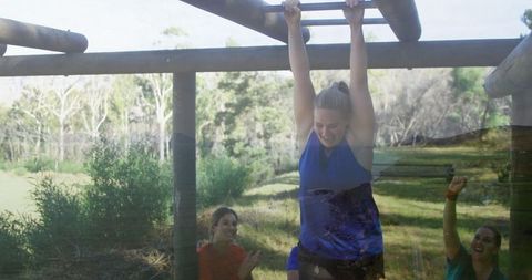 Woman gripping monkey bars while friends cheer in triumphant outdoors scene