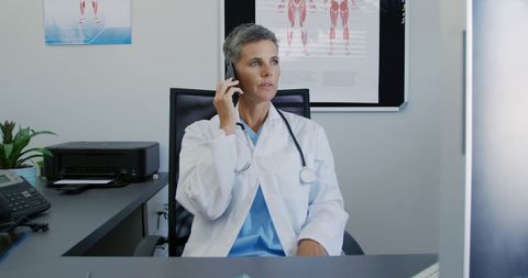 Caucasian female doctor making important phone call at office desk