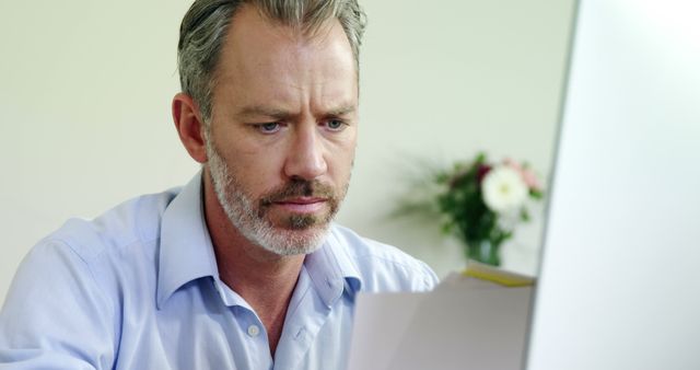 Man analyzing documents on computer at desk. Suitable for businesses, financial services, consultant services, entrepreneurial endeavors, corporate training materials, and professional presentations.