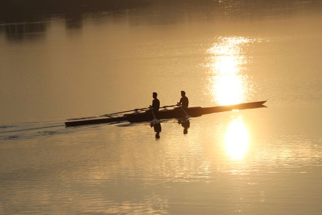 Two individuals paddle a canoe on calm water during sunset, creating a serene and peaceful scene. Perfect for use in travel, adventure, motivational, and nature-themed designs, as well as promoting outdoor activities and teamwork.