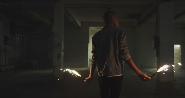 Person holds sparklers in dark industrial building, creating a mysterious and celebratory atmosphere. This image is ideal for themes of mystique, urban exploration, night-time celebrations, or those showcasing abandoned spaces with a dramatic twist.