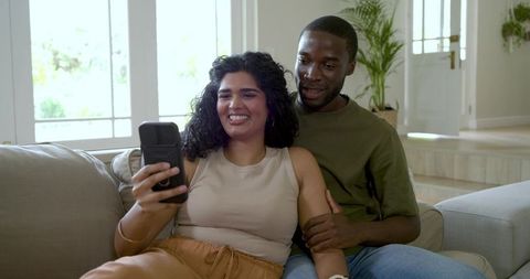 Couple taking vertical selfie on sofa, recording social media video, smiling partners at home