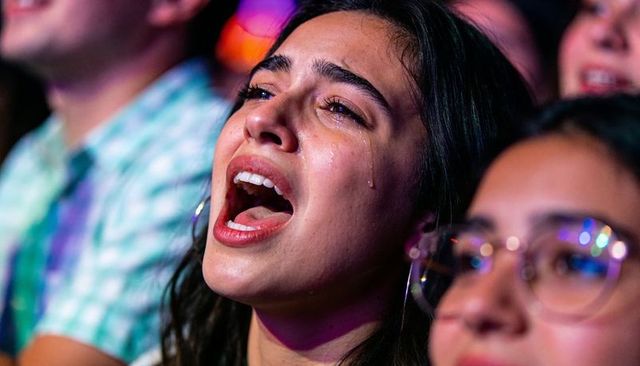 Tearful woman singing passionately in crowd at live concert under dramatic stage lights