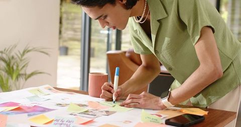 African American woman leaning over table labeling colorful sticky notes for planning