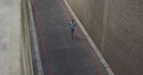 Solo urban runner jogging through narrow brick alleyway on overcast day for fitness