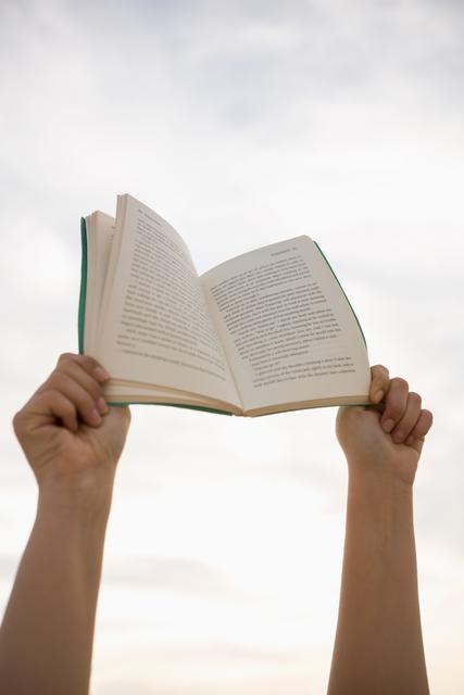 Hands holding an open book against a bright, sunny sky. Ideal for themes related to reading, education, outdoor activities, relaxation, and inspiration. Suitable for use in educational materials, book promotions, and lifestyle blogs.