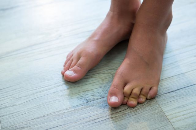 This image shows a child's bare feet standing on a wooden floor. It can be used in contexts related to home life, childhood, flooring materials, or health and wellness. Ideal for articles, blogs, or advertisements focusing on home decor, family life, or foot care.