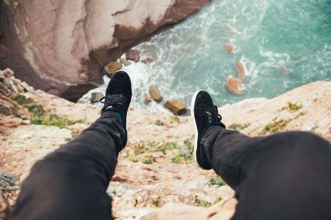 Adventurous Man Dangling Legs Over Rocky Ocean Cliff