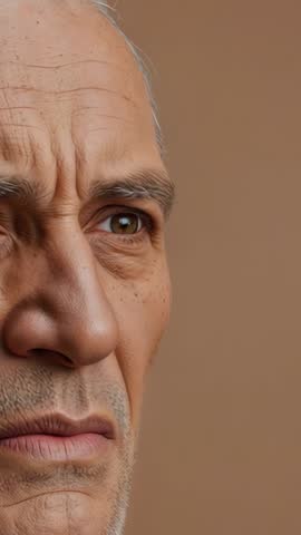 Vertical close-up of older man contemplating on beige backdrop for introspective video