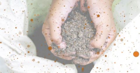 Cupped small bare hands holding dry mulch on white fabric with orange-brown speckle overlay