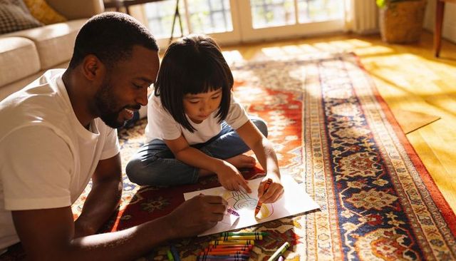 Father and child coloring together on sunlit living room rug sharing joyful family bonding