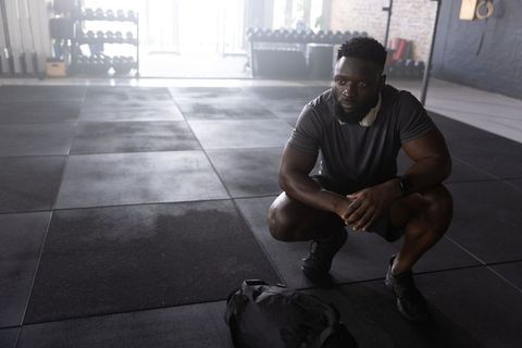African american athlete squatting in industrial gym resting after strength training session