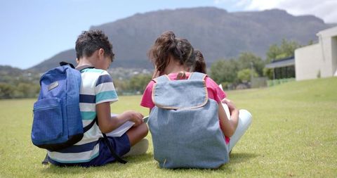 Children Sitting on Grass Facing Mountain with Backpacks, School Break