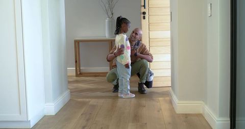 Father kneeling hugging african american daughter in wooden hallway by front door