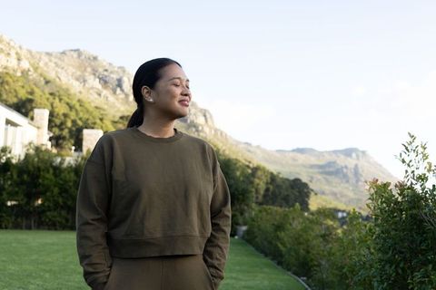 Mid-adult asian woman standing relaxed on manicured lawn with mountain and garden view
