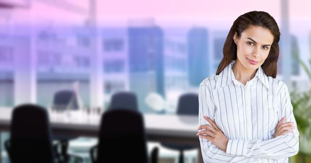 A confident businesswoman stands in a modern office with arms crossed, dressed in a white shirt, showcasing professionalism and successful career. Ideal for use in corporate websites, business presentations, career guides, and professional development materials to emphasize leadership and confidence in a corporate environment.