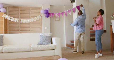 African American Couple Hanging Purple Garland and Balloons in Modern Living Room