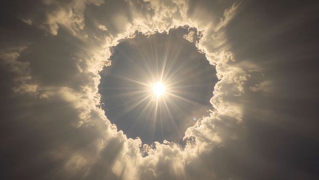 Sunburst radiating through circular cloud aperture, dramatic rim-lit sky crepuscular rays