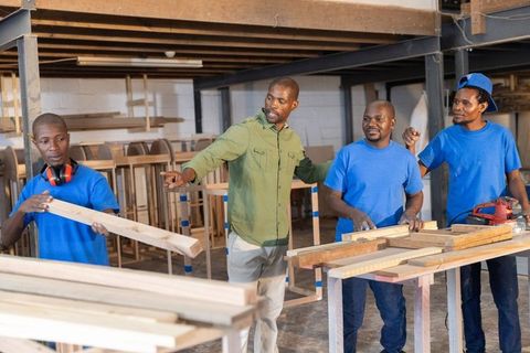 African american team collaborating in woodworking workshop, handling lumber and tools