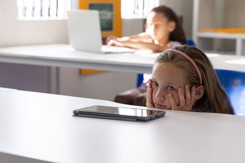 Bored schoolgirl resting chin on hands while waiting for class with tablet on desk