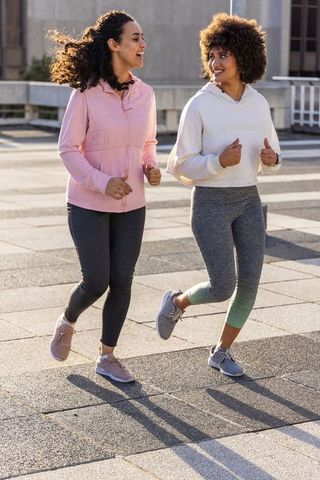 Two women jogging together on urban rooftop plaza at sunrise smiling and exercising