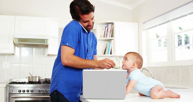 Father multitasking in a kitchen by feeding his baby from a bottle while simultaneously working on a laptop. Presents modern parenting, work-life balance, and family life zuggesting use for articles or advertisements related to parenting tips, work-from-home guides, family technology, and lifestyle blogs.