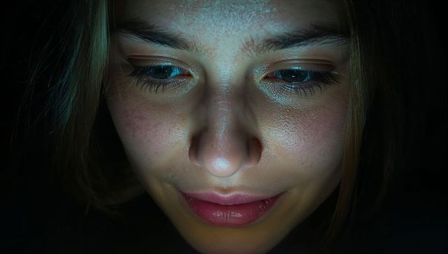 Gazing young woman at screen with blue glow closeup intimate low-light portrait
