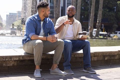 Diverse friends chatting by urban fountain holding coffee cups casual sunny conversation