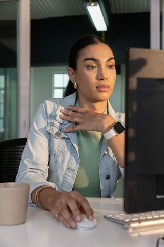 Focused professional woman working at modern office desk using wireless mouse and smartwatch
