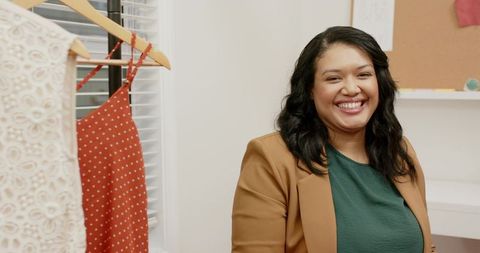 Smiling boutique stylist beside clothing rack featuring polka dot dress and lace dress