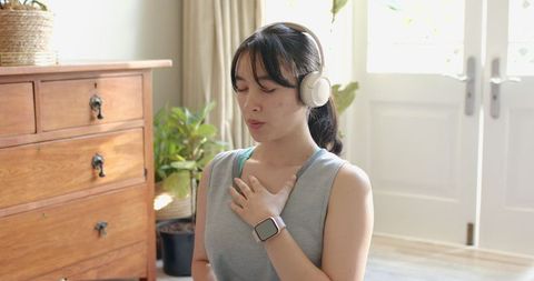 Asian woman meditating with headphones in bright living room