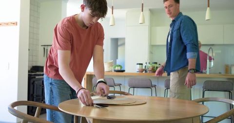 Teen arranging woven placemat while father watching in modern open-plan kitchen