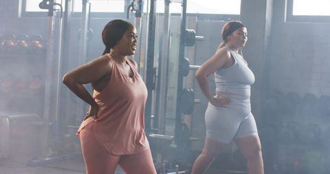 Plus-size black women working out together performing lunges in industrial gym