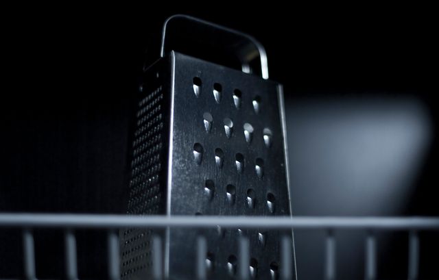 Close-up of stainless steel box grater seen on black background. Perfect for use in articles or advertisements related to cooking, kitchen utensils, and food preparation. Ideal for educational content, cooking blogs, e-commerce sites, or product catalogs focusing on household or kitchen items.