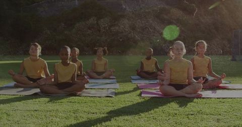 Children practicing outdoor yoga meditation on sunlit field in yellow tops